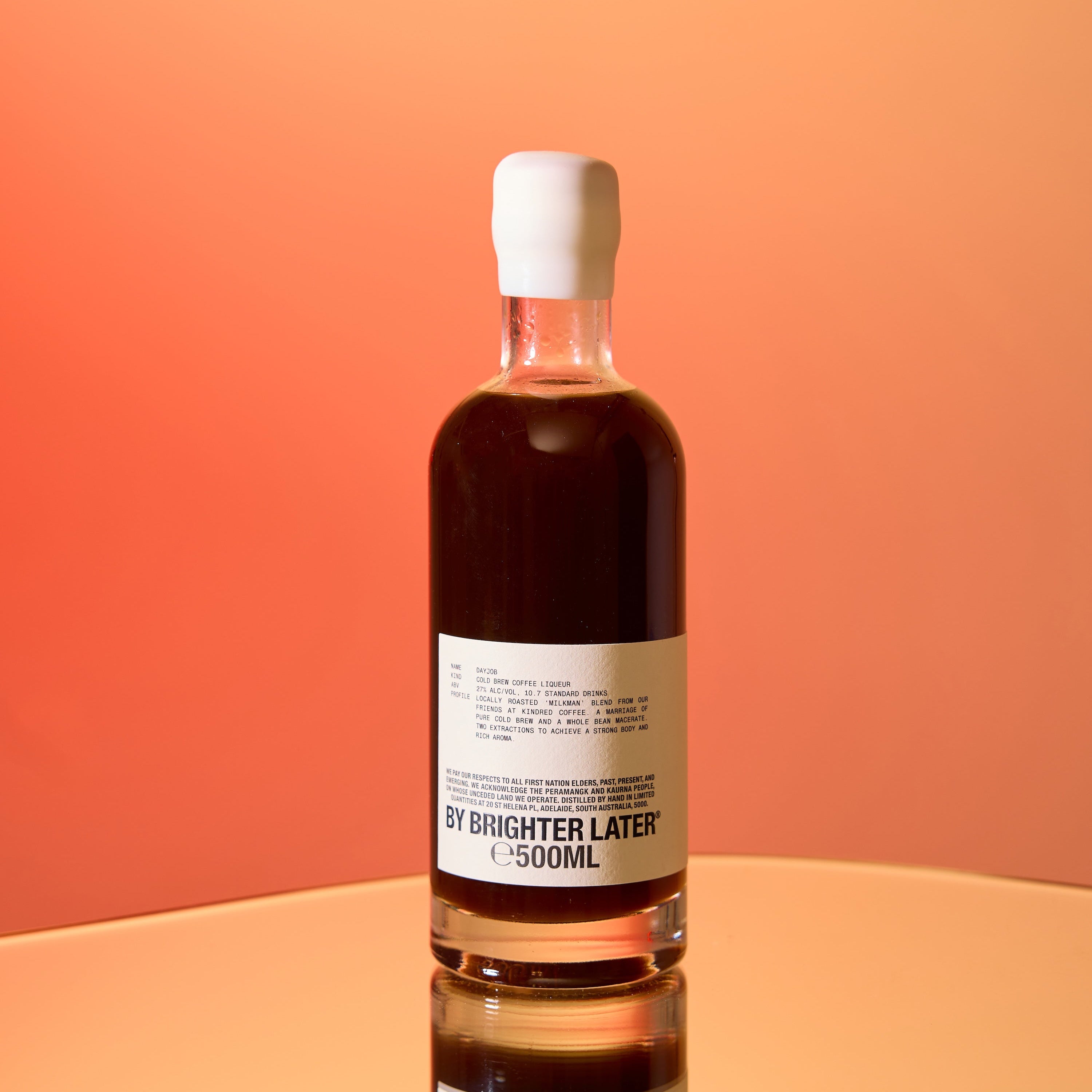 A bottle of coffee liqueur on a sunset orange gradient studio background.