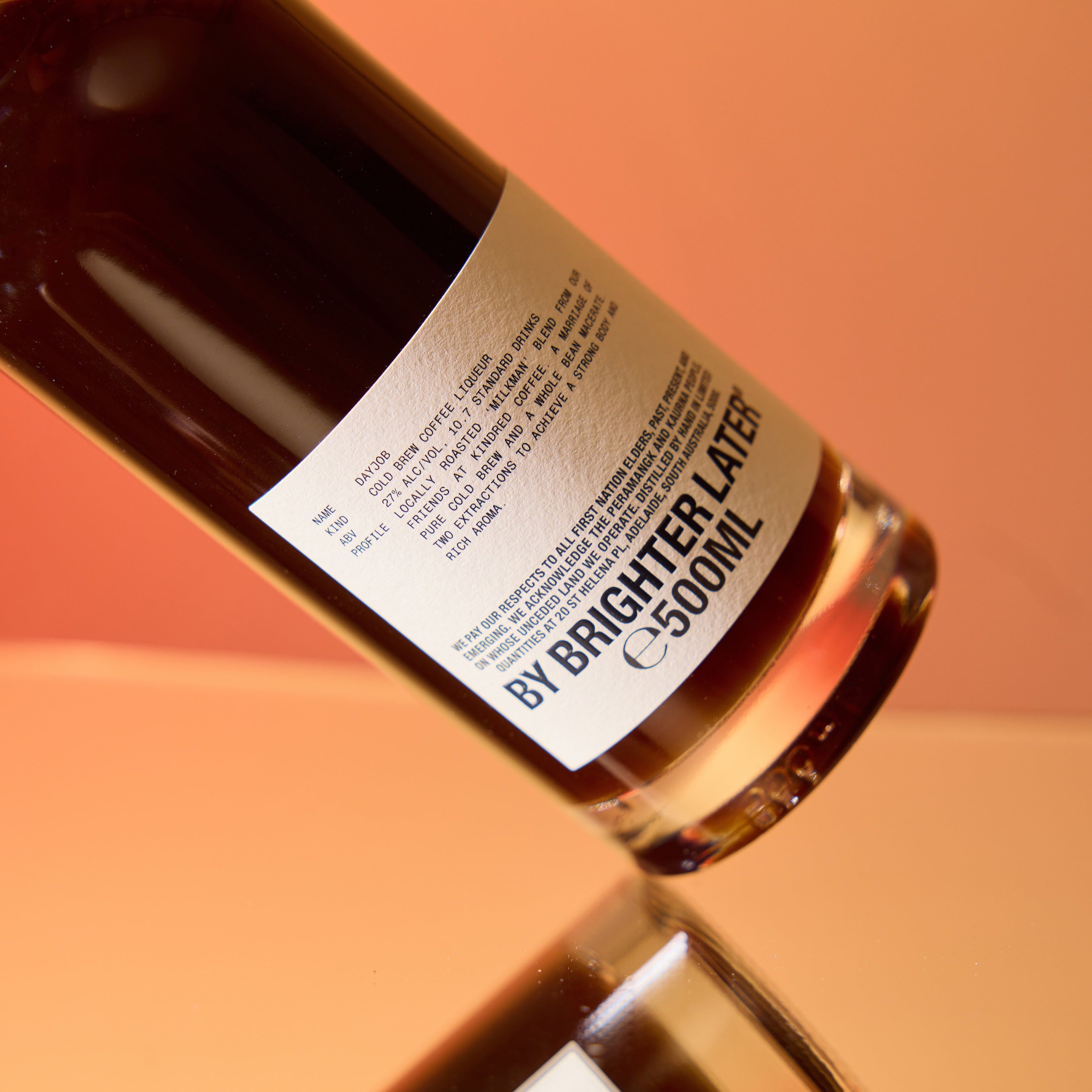 A bottle of coffee liqueur on a sunset orange gradient studio background.